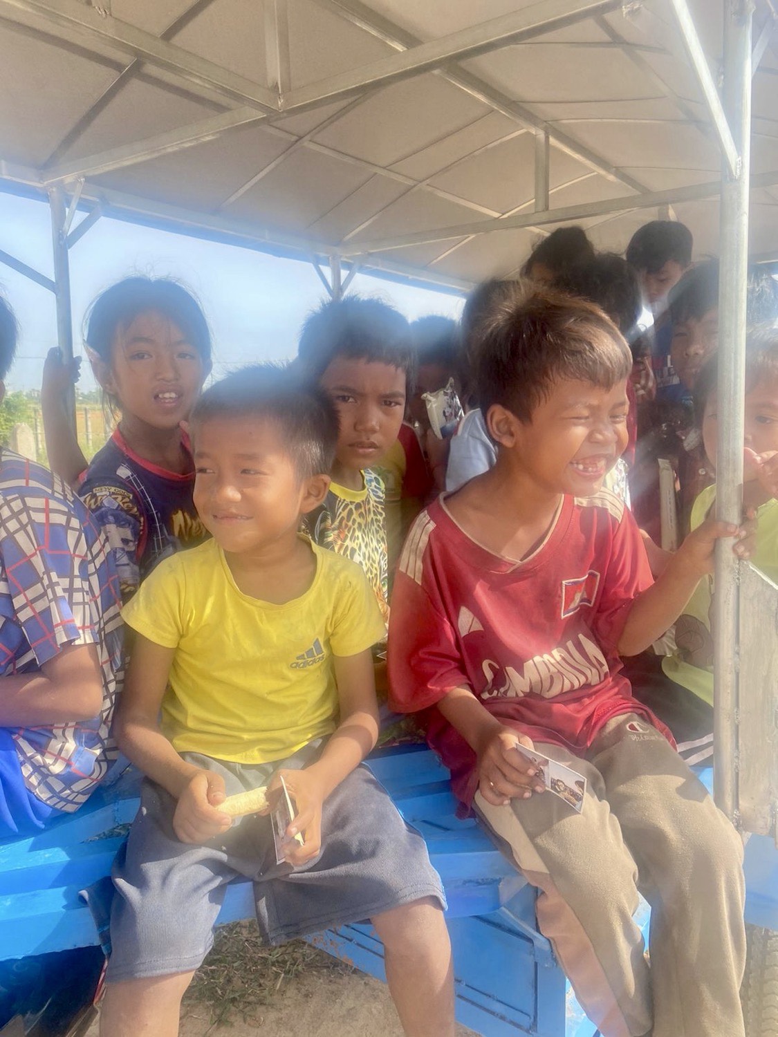 Children sitting together on a bench outdoors, laughing during a lesson