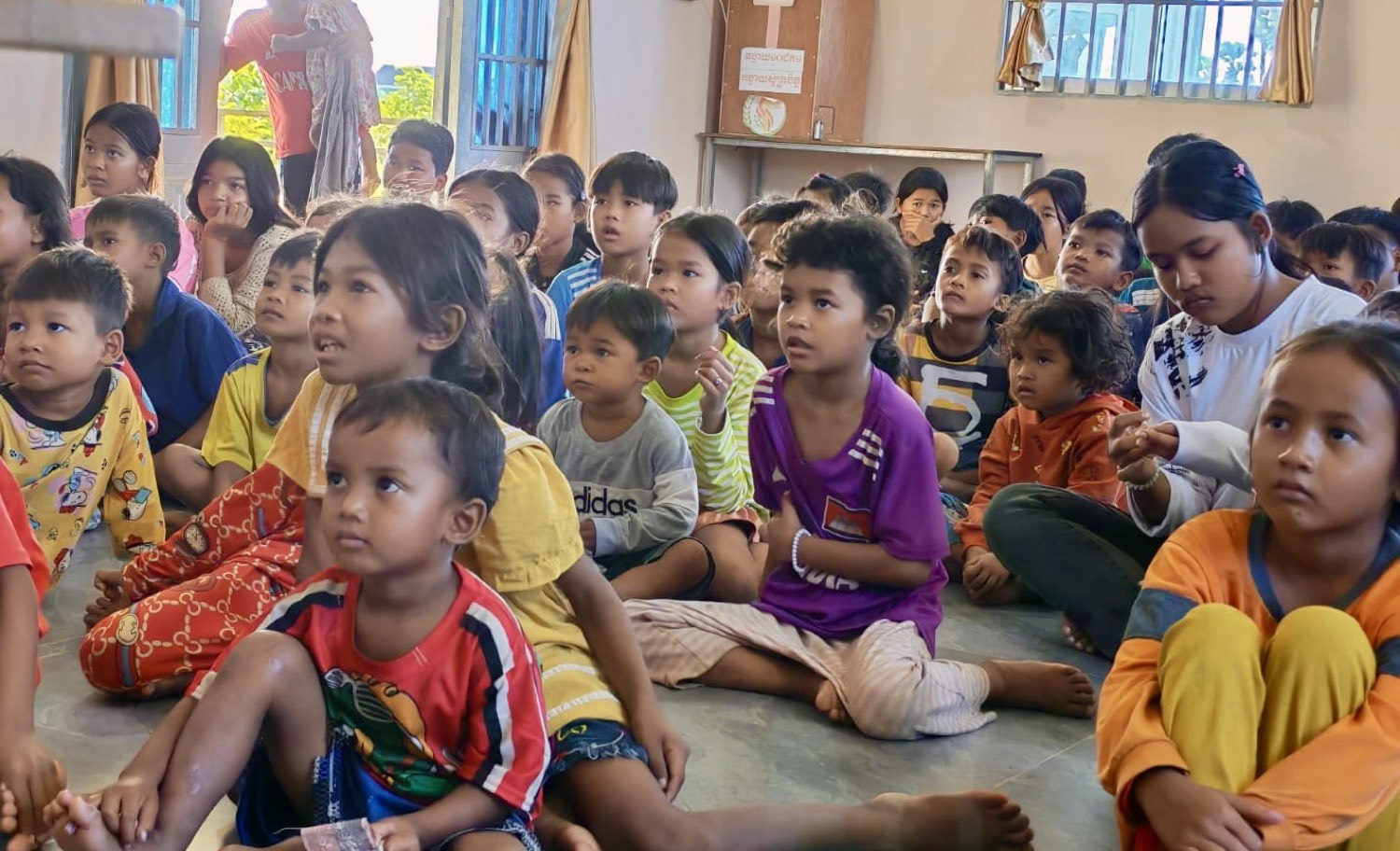 A room full of children sitting on the floor, listening during a lesson