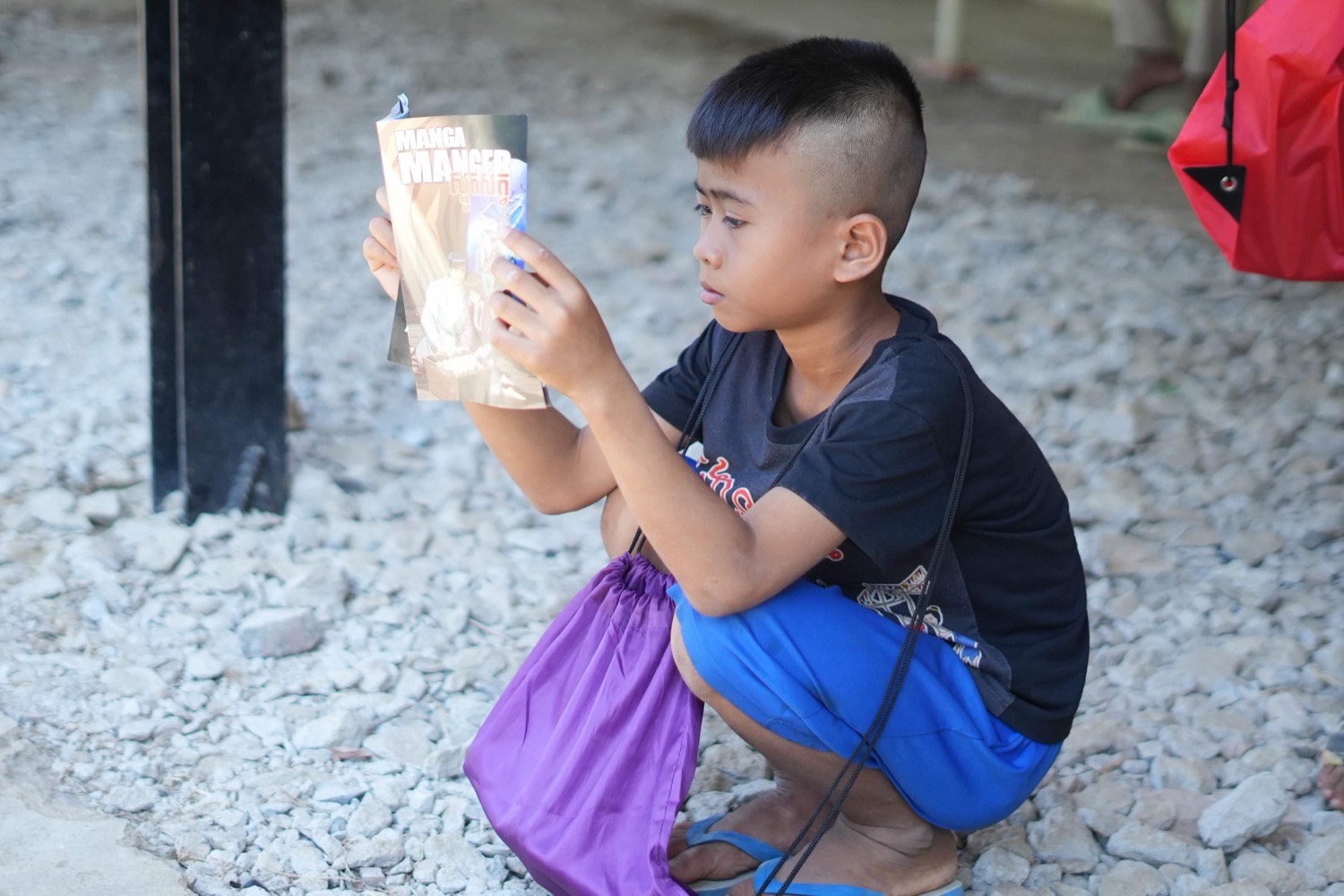 A boy crouching outside, absorbed in reading a book