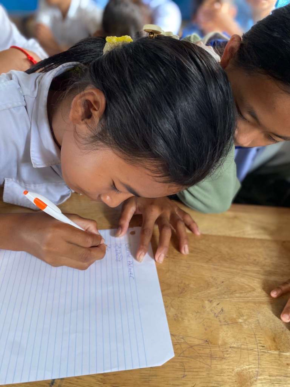 A girl in a school shirt writing carefully on lined paper