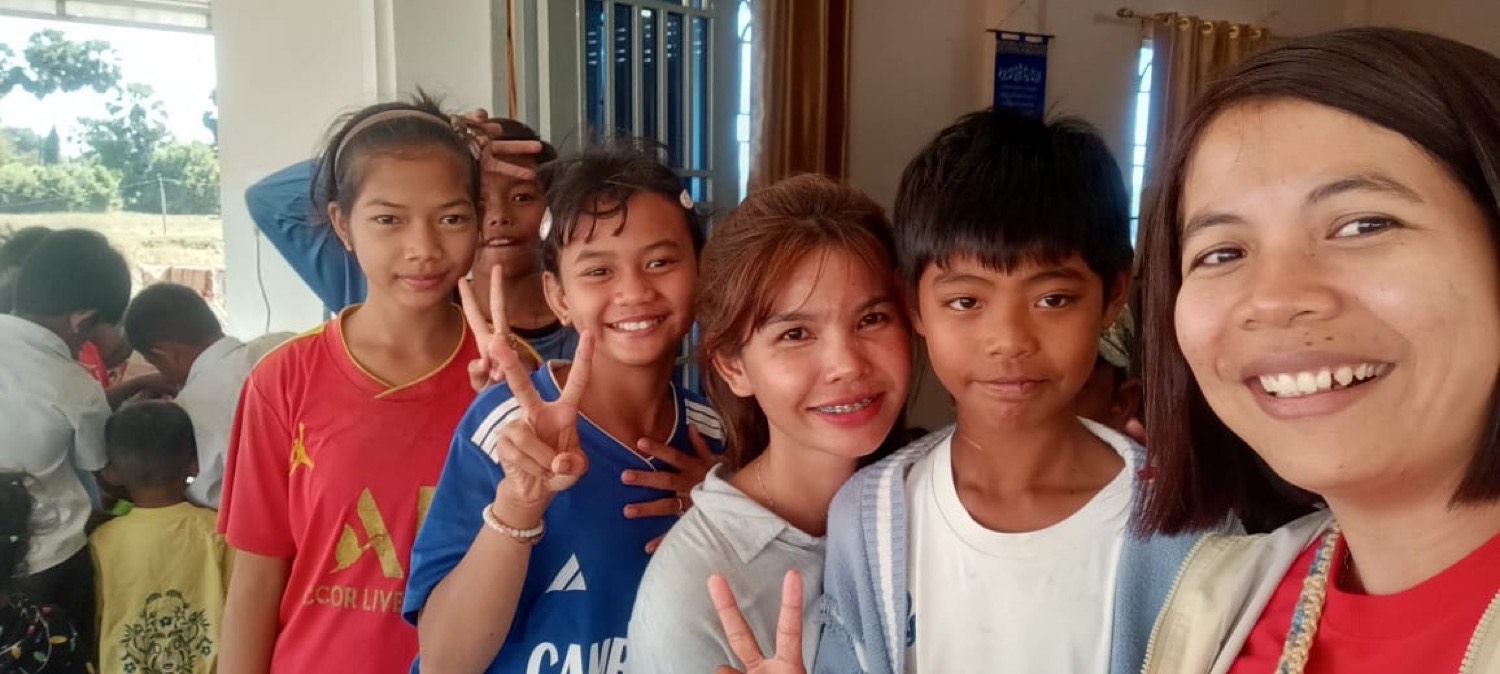 A Light of Cambodia teacher smiling with a group of students