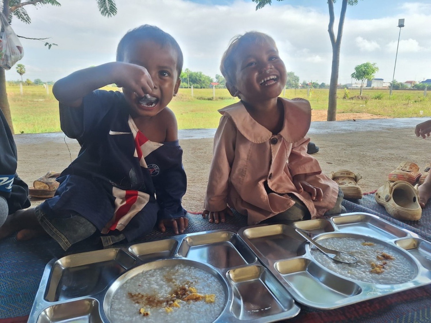 Two small children grinning over trays of rice at the daily meal