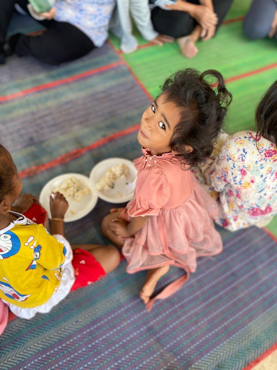 A young girl in a pink dress looking up from her plate during the meal