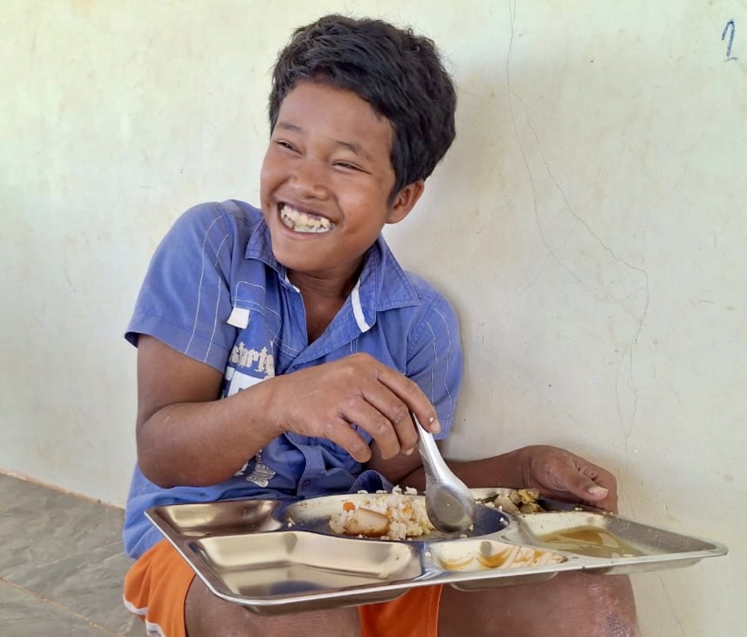 A boy grinning over his tray of rice and vegetables at the daily meal