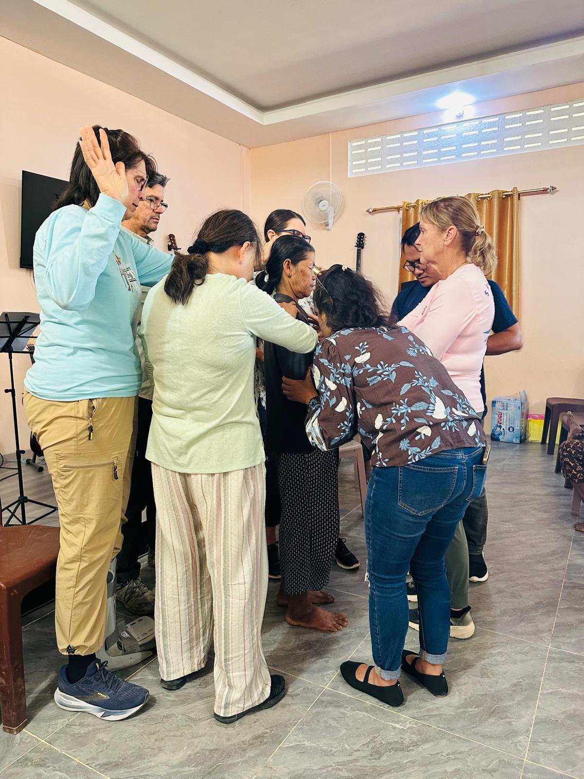 Church leaders standing in a circle with hands laid on one another in prayer during a leadership training session in Pursat