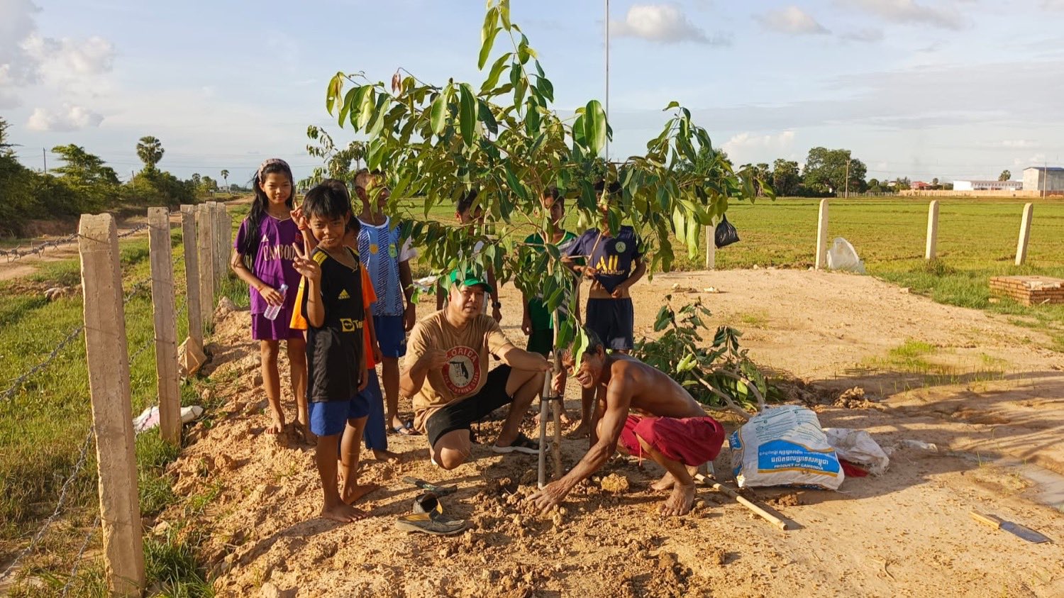Local staff and children planting a young shade tree on the ministry property