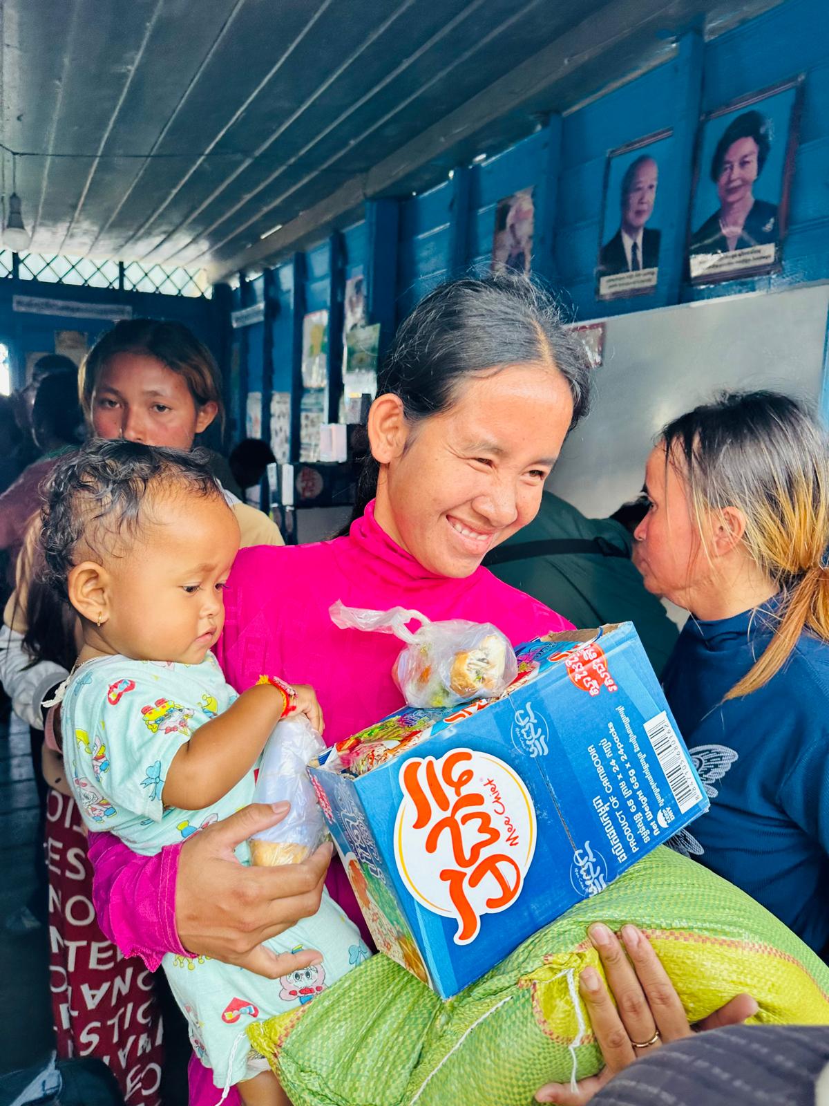 A mother holding her child while receiving a box of food and a sack of rice