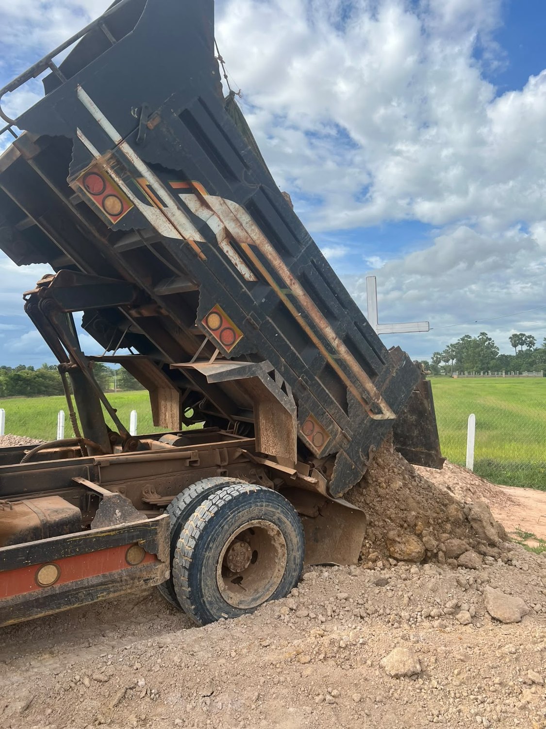 A dump truck tipping a load of soil onto the ministry property, with rice fields behind